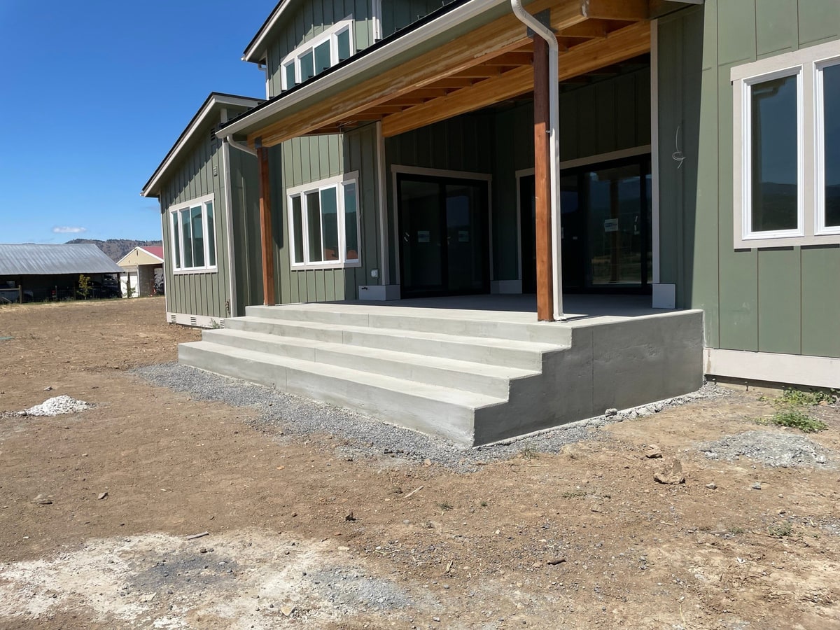 Back porch with wide concrete steps at a green farmhouse-style home.