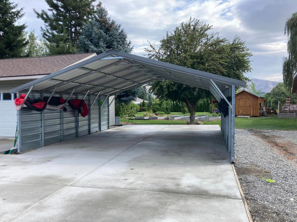 Metal carport with a new slab, trees and a small shed behind.