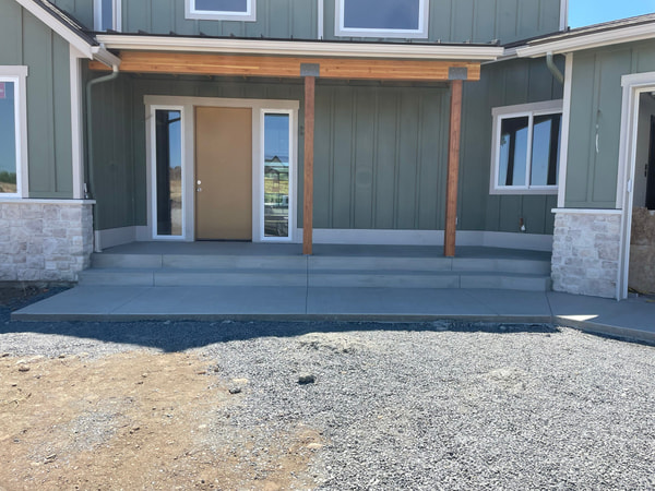 New front entry porch slab at a green board-and-batten house with stone columns.