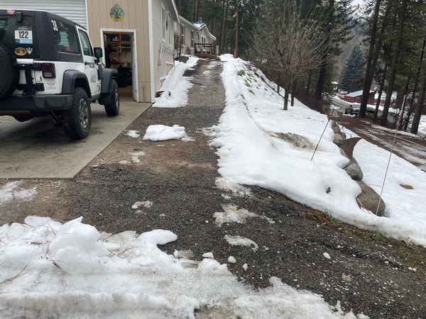 Jeep parked on a snowy gravel drive by the garage.
