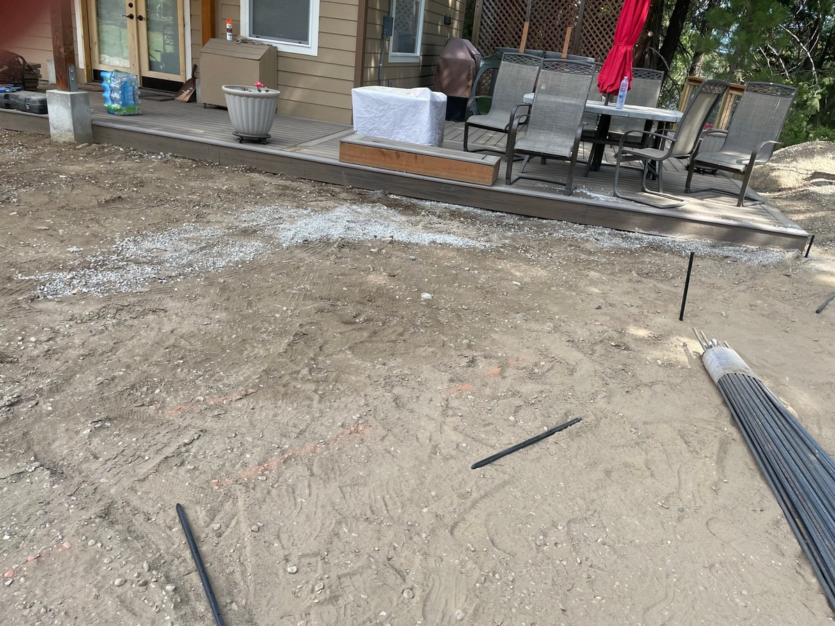 Dirt patio area with rebar bundles and a deck with furniture.
