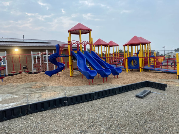 Red, blue and yellow play structure on wood chips with a black border.