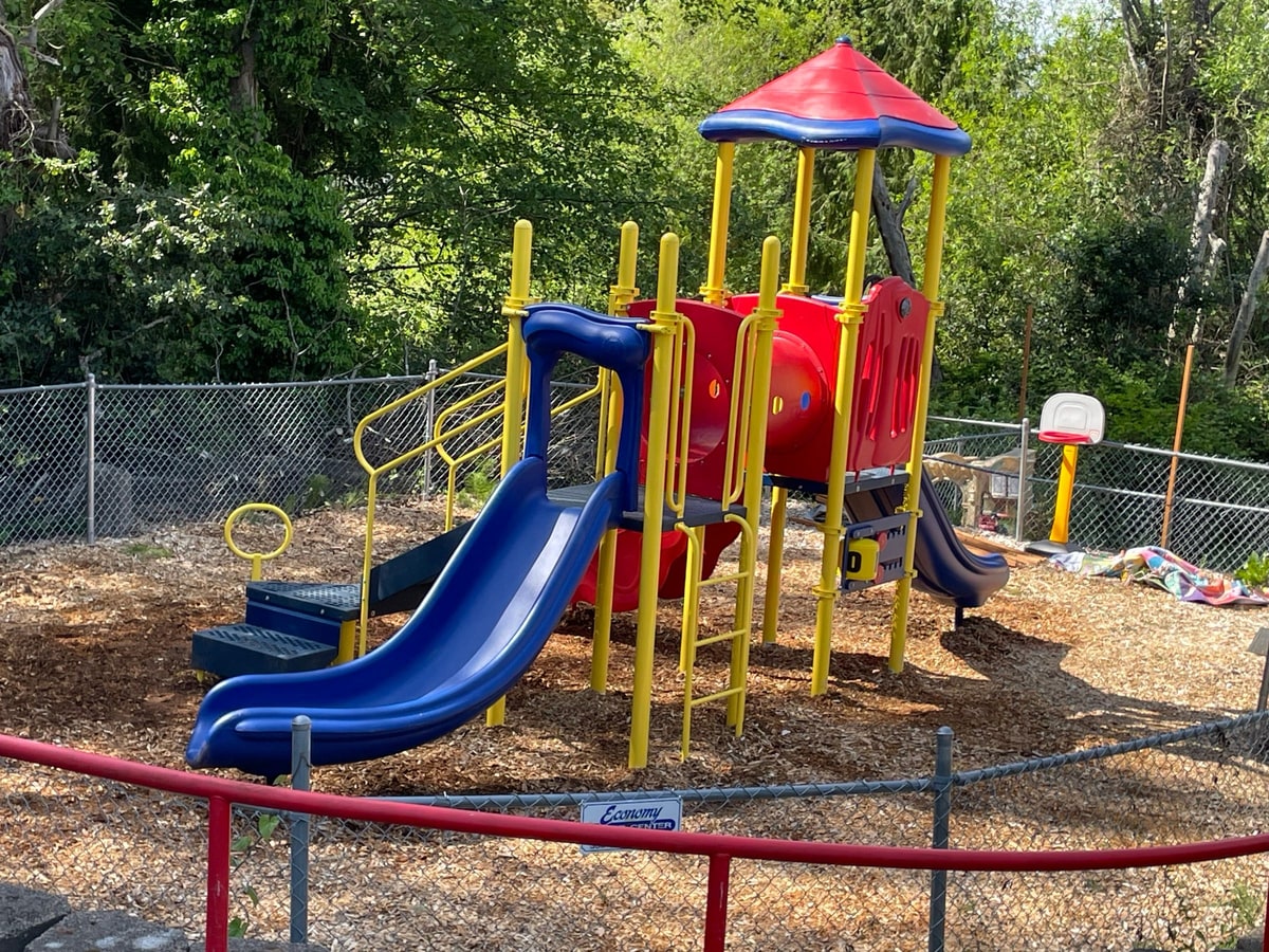 Play structure on wood chips seen over a red fence rail.