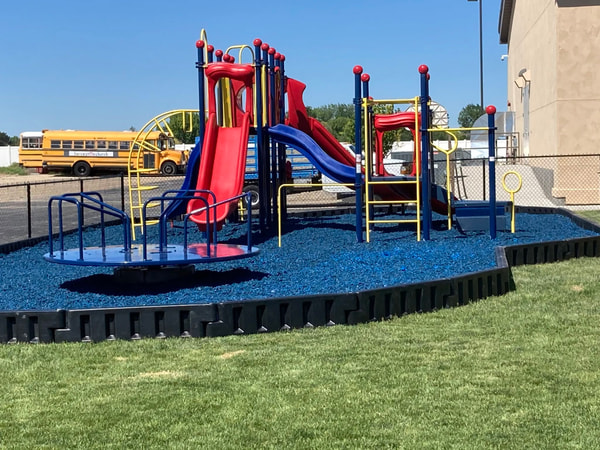 Playground on blue rubber mulch with a school bus in the lot.