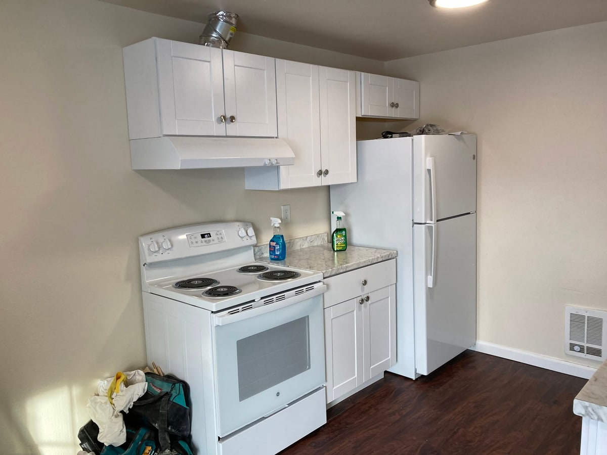Kitchen with white cabinets, range hood, stove and fridge.