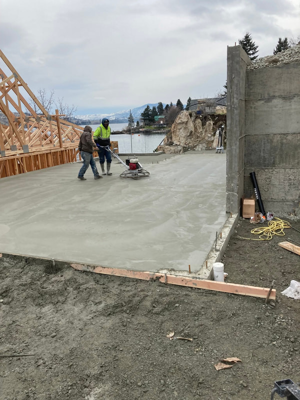 Crew finishing a large foundation slab with framing behind.