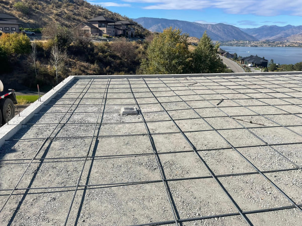 Rebar grid over gravel with Lake Chelan and hills beyond.